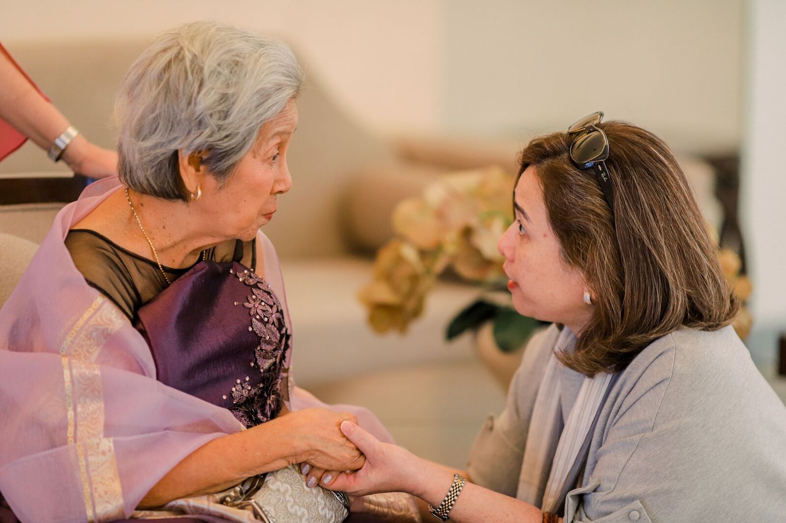 An older woman and a younger woman holding hands during a conversation at home